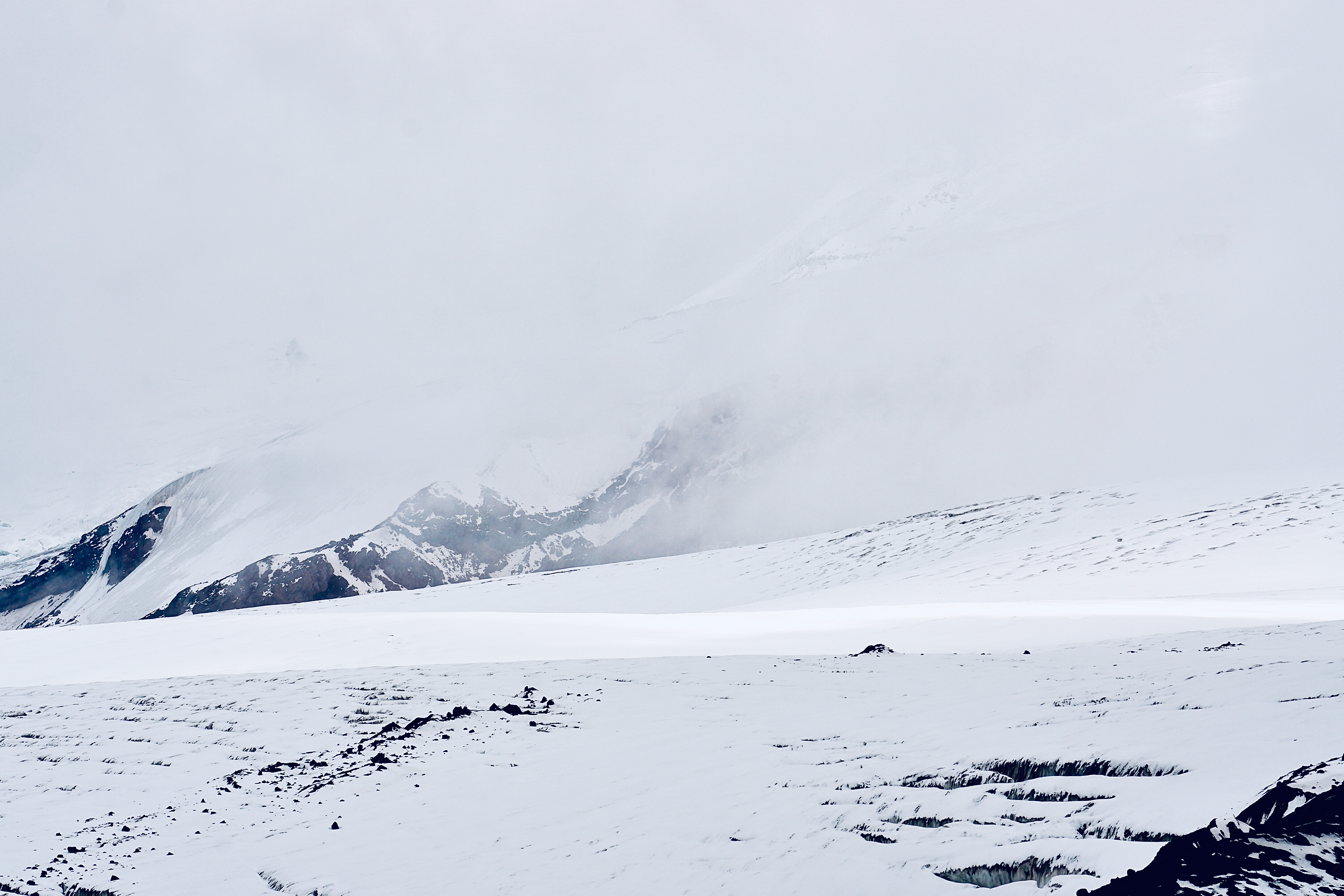 Un amplio glaciar alpino y picos nevados bajo cielo nublado.