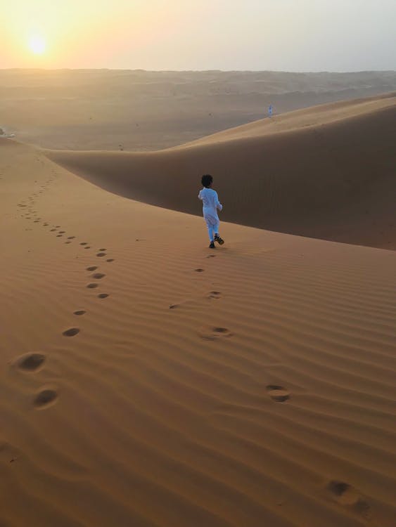 Vista Posteriore Foto Di Un Ragazzo Musulmano In Thobe Bianco Che Cammina Da Solo Sulla Sabbia Del Deserto Durante L'ora D'oro