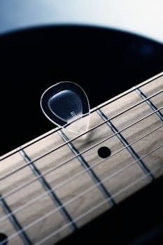 Vertical shot of a guitar pick resting on musical instrument strings, highlighting musical themes.