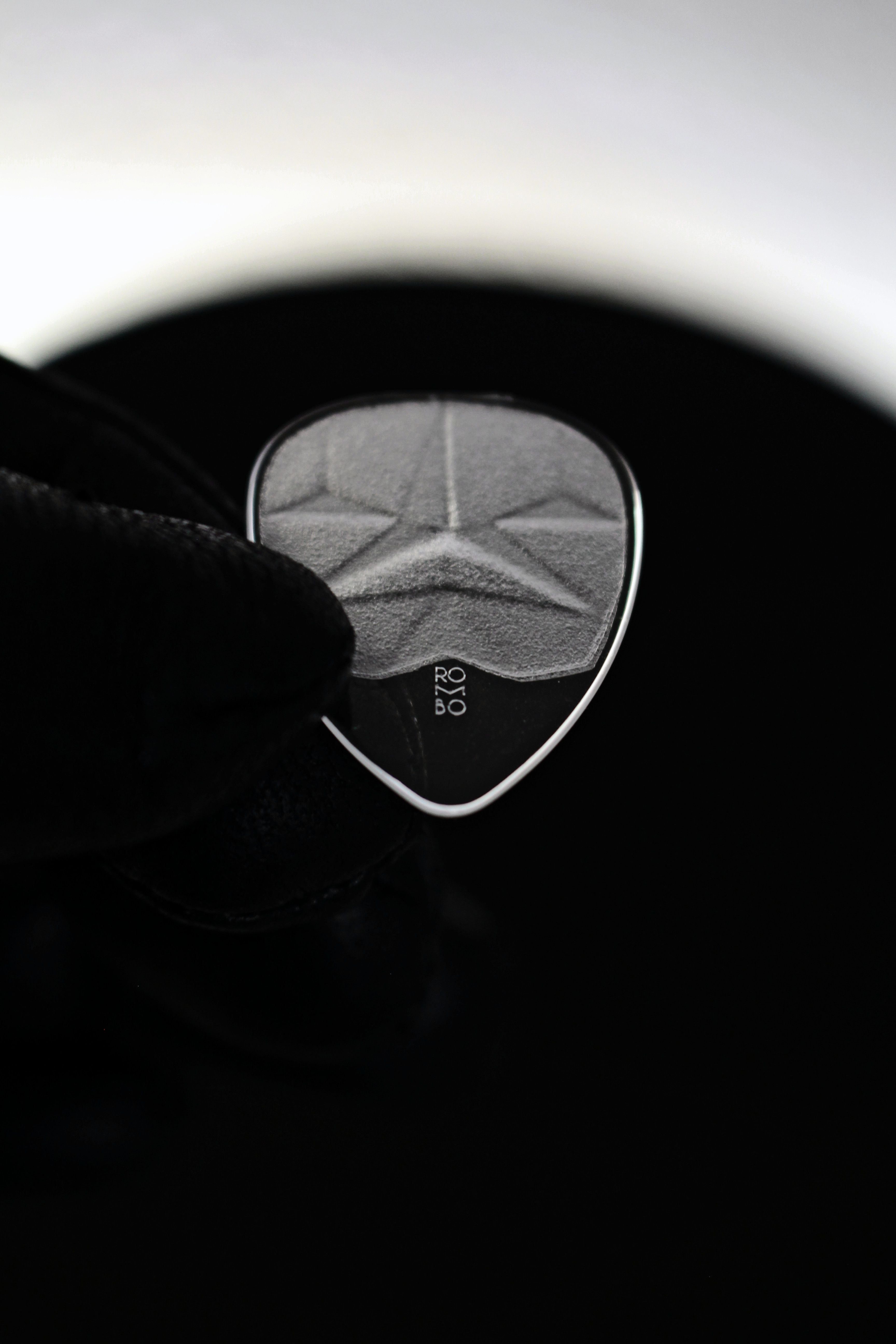 Detailed image of a modern black guitar pick against a dark background.