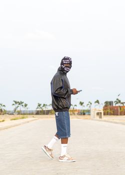 Young adult in streetwear style using a smartphone outdoors, showcasing modern urban fashion.