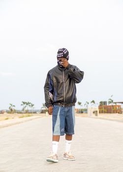 Man in streetwear style with hat and jacket on an empty road.