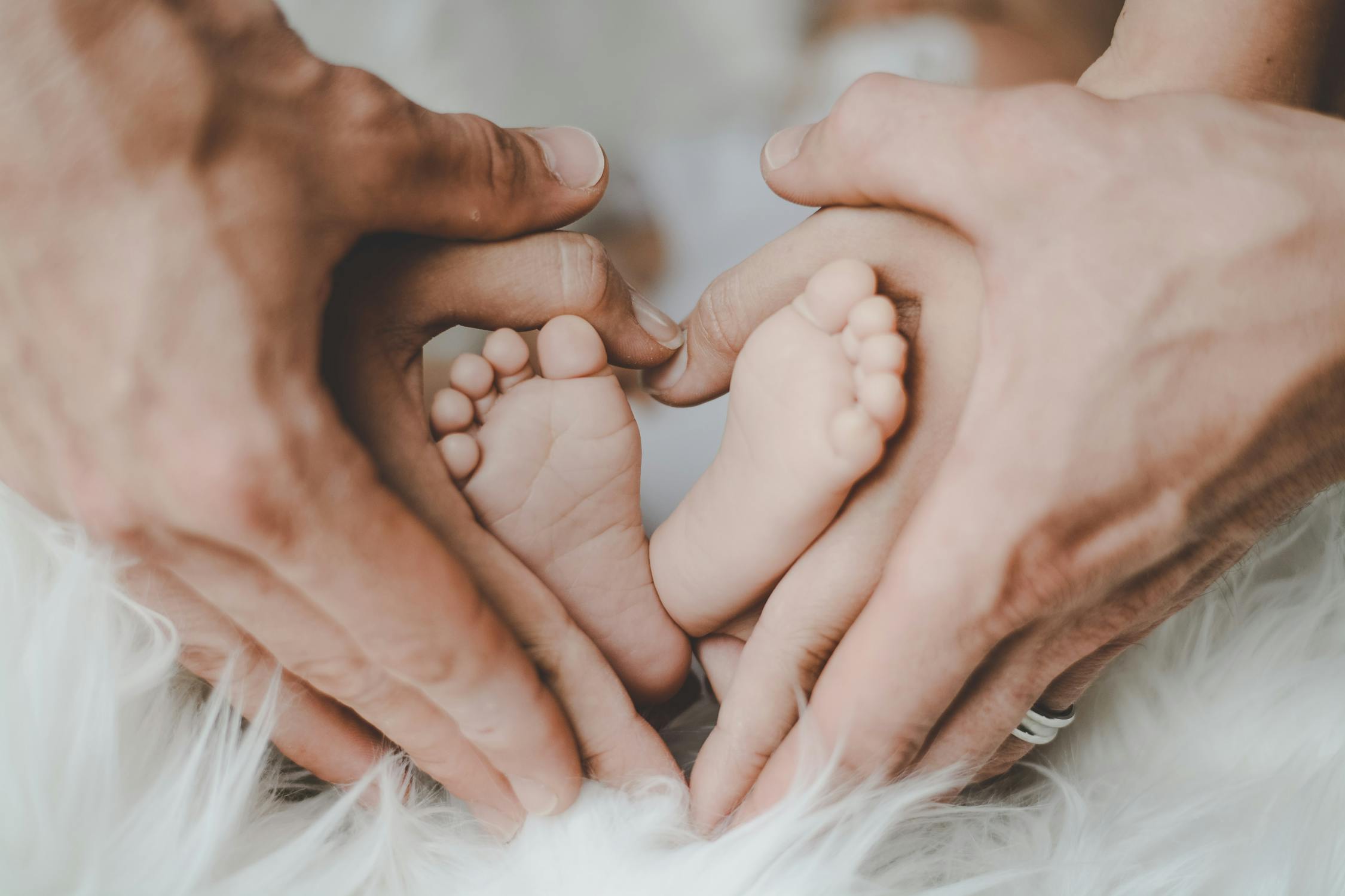 A close-up of two parents’ hands forming a heart around their baby’s feet.