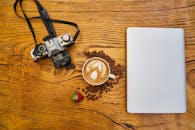 木桌上摆放着老式相机、咖啡和笔记本电脑，草莓放在上面