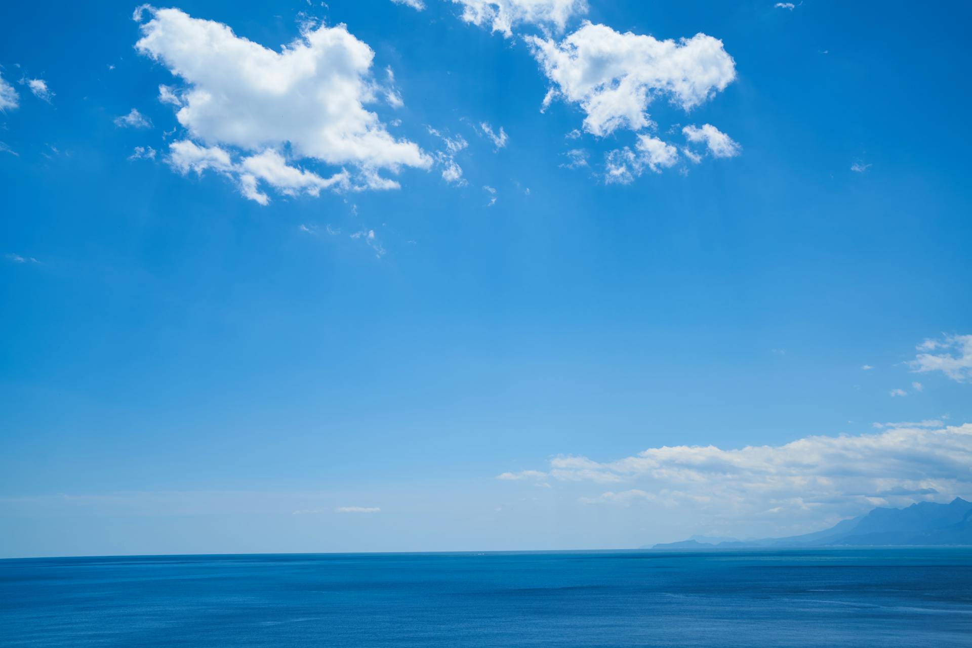 A wide expanse of calm ocean meets the bright blue sky with scattered clouds on a clear day.