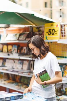 一位女子在一家挂着五折标志的户外书店里，手里拿着几本书在购物