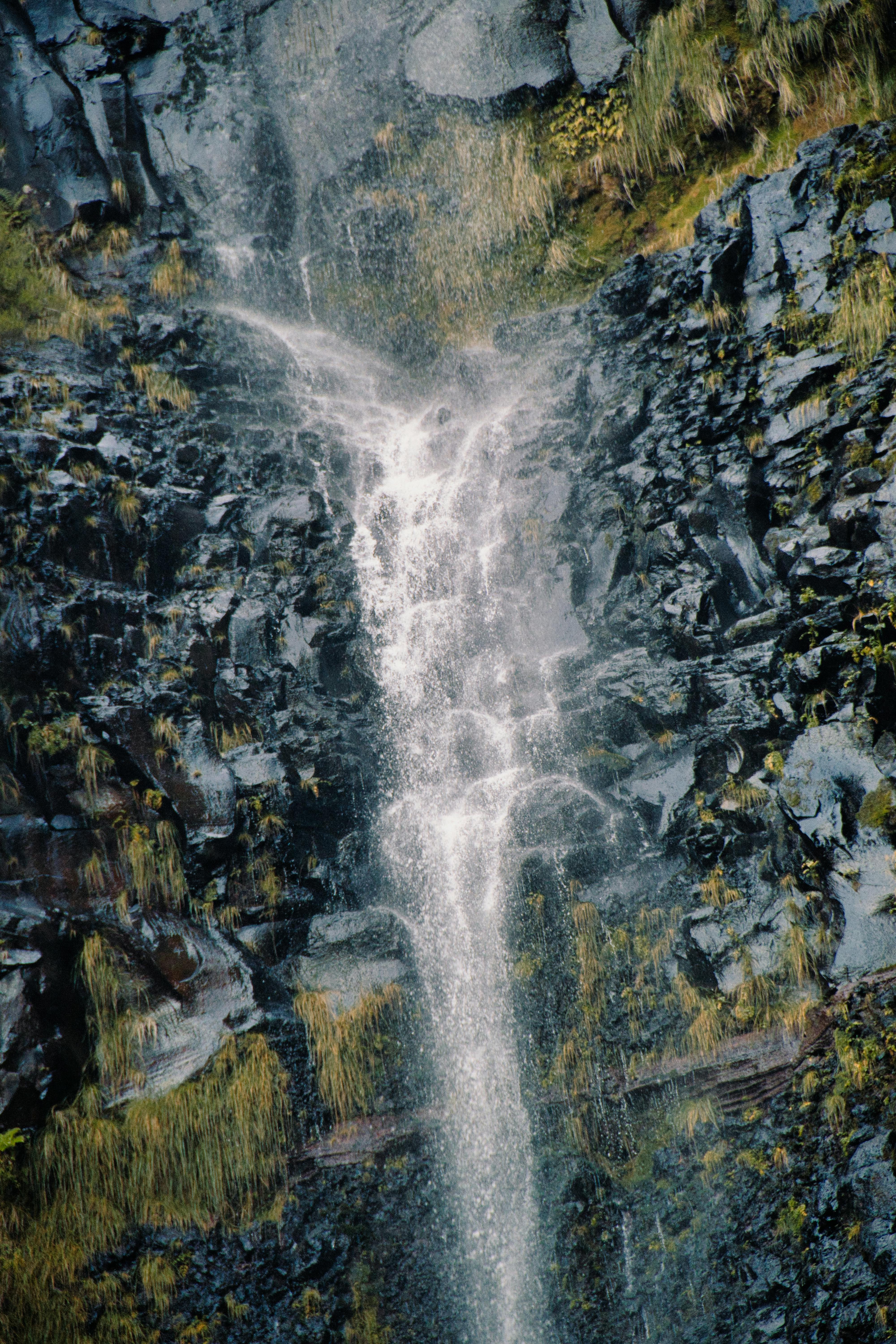 Beautiful waterfall cascading over a rocky cliff, surrounded by lush vegetation in Madeira, Portugal.