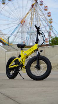 Bright yellow electric bicycle with fat tires in front of an amusement park ferris wheel