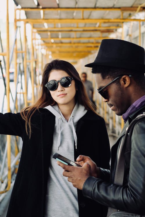 Free Smiling Woman Standing Beside Man Using Smartphone Stock Photo