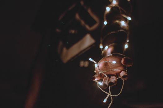 A close-up of a hand wrapped with warm glowing string lights in the dark.