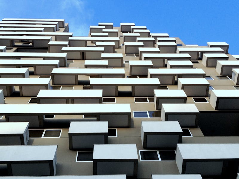 Low angle view of a modern building with geometric patterns and staggered balconies against a clear blue sky.
