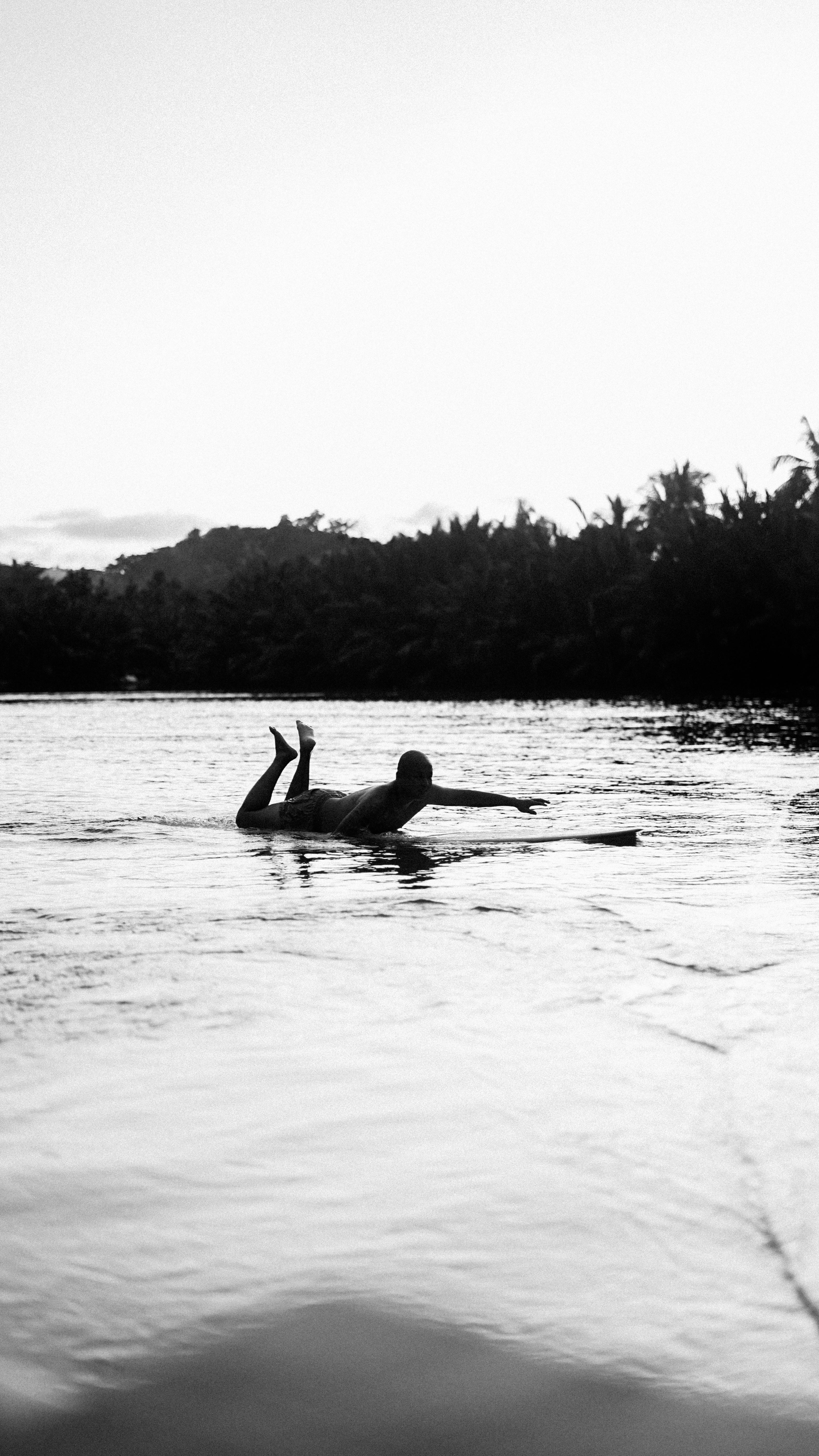 Silhouette of a surfer paddling on a board during a serene sunset.