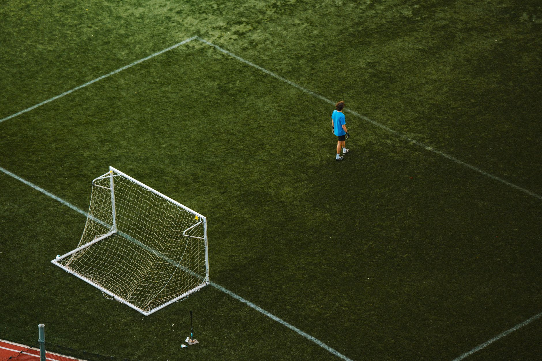 Aerial view of a lone soccer player near a goalpost on a grassy field.