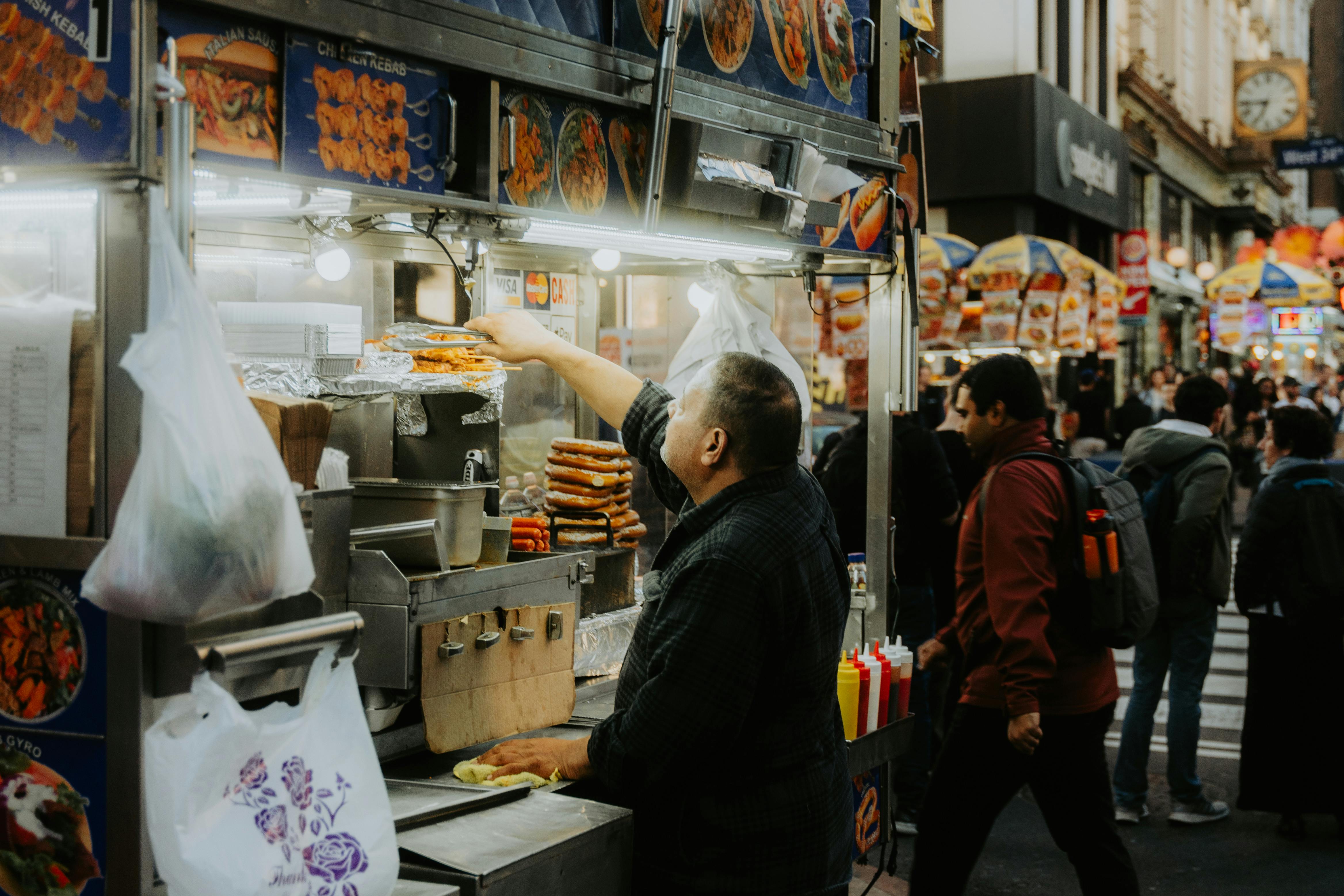 Street vendor serves customers at busy food stand in city alley.
