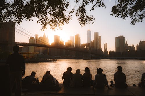 People sitting on a bench near the brooklyn bridge at sunset