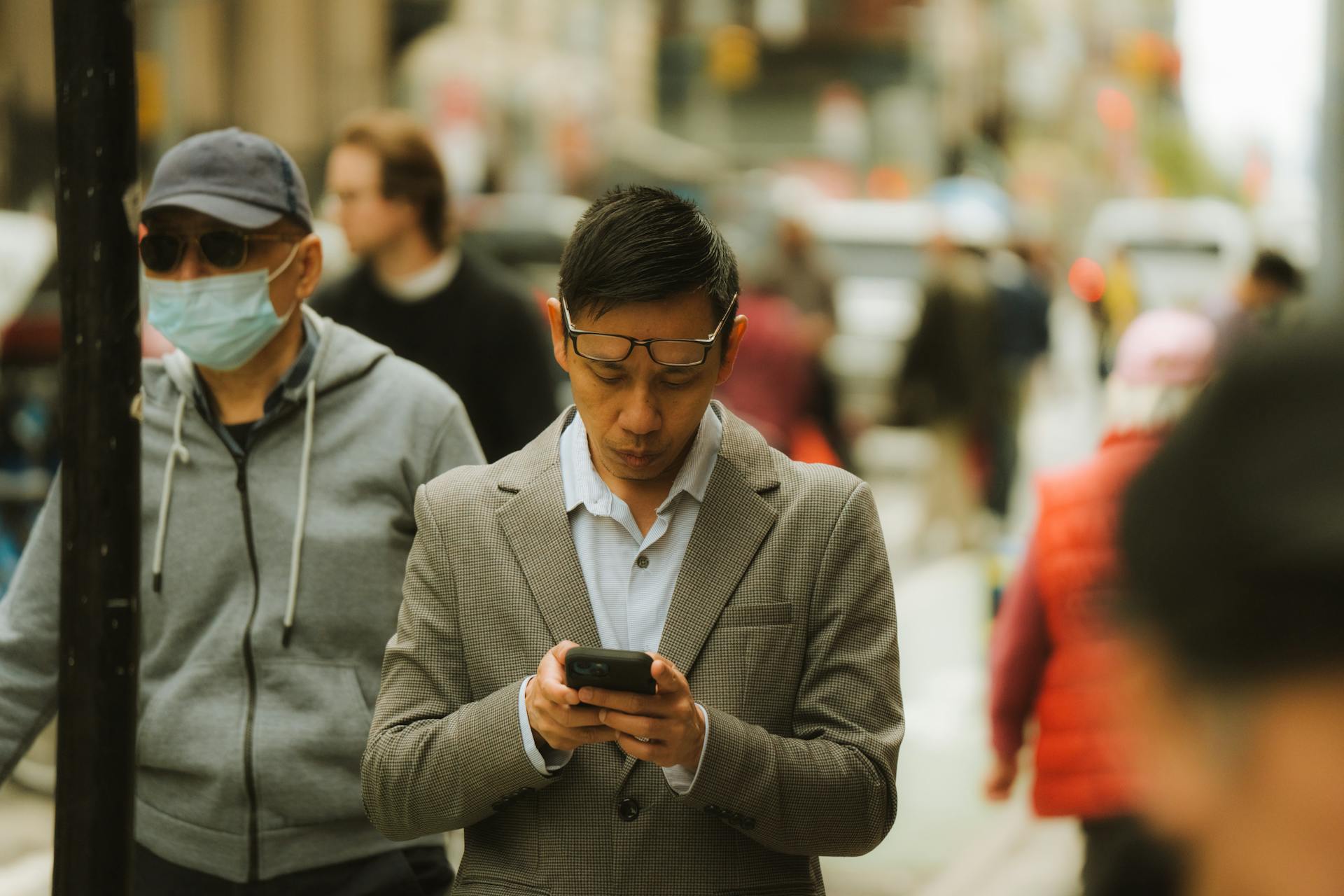 A businessman in a suit checks his smartphone while walking down a busy city street.