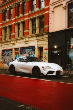 White Toyota Supra parked on a vibrant city street, showcasing urban architecture.
