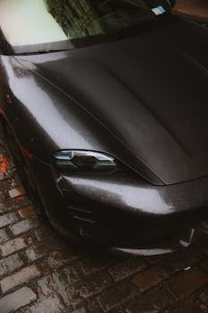 High-angle view of a black sports car on a rain-soaked cobblestone city street.
