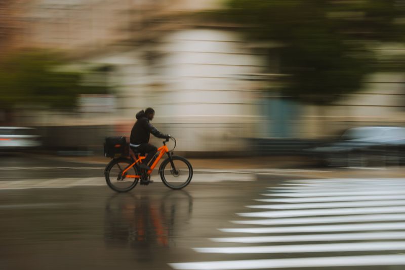A fast-moving cyclist rides through rainy city streets, capturing motion and energy.