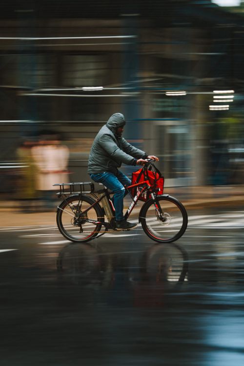Free Man rides a bicycle on wet city streets during rain, creating a dynamic urban scene. Stock Photo