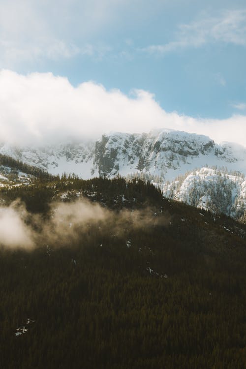 A mountain covered in snow and clouds with a blue sky