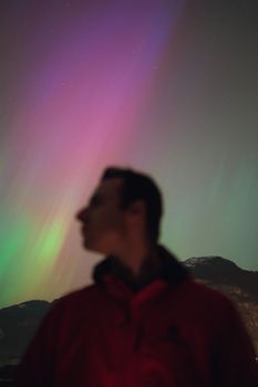 Defocused silhouette of a hiker under the vibrant aurora borealis at night.