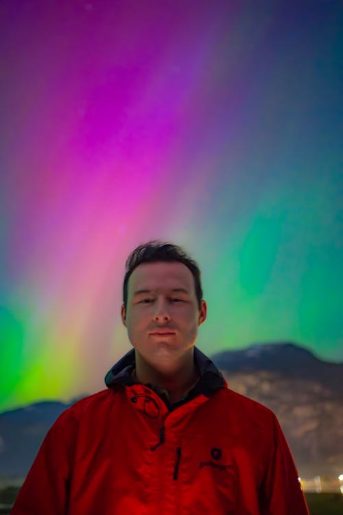 A man standing in front of a colorful aurora bore