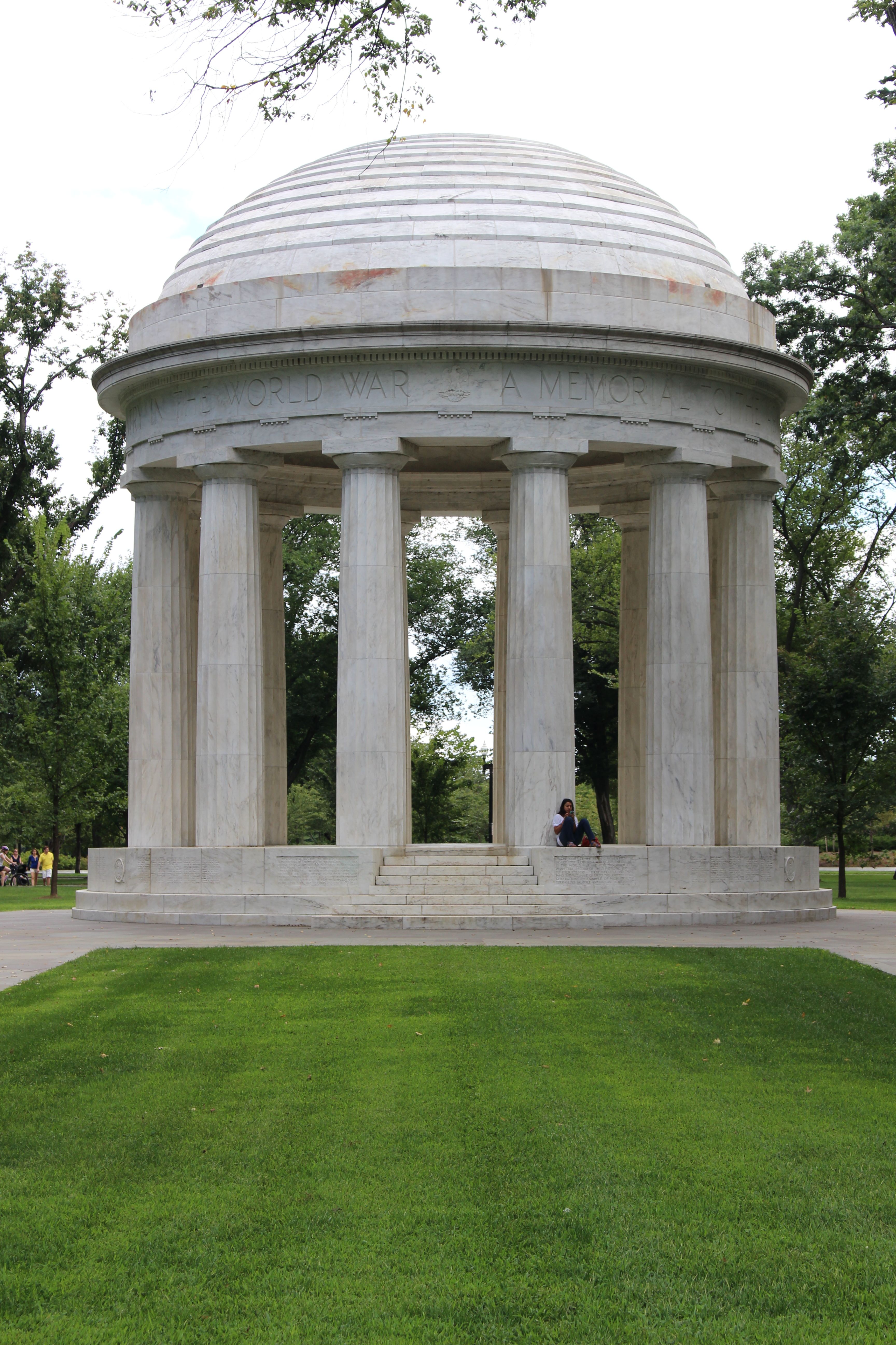 Vista do Memorial da Segunda Guerra Mundial no National Mall em Washington, Estados Unidos, com arcos de pedra, elementos de fonte e um cenário de parque formal.
