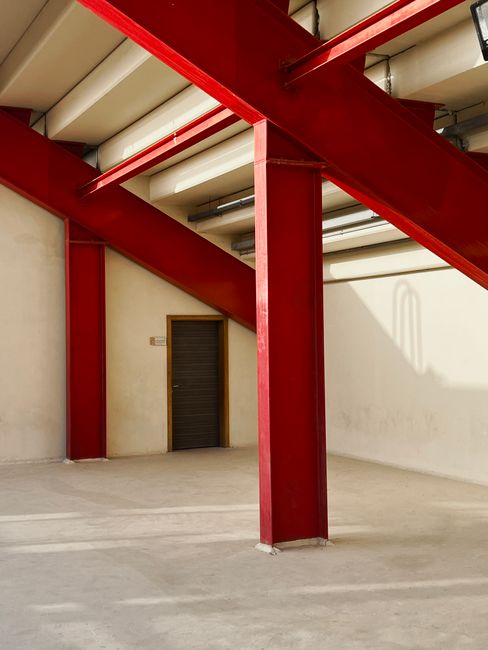 Interior view of a sunlit industrial space with red support beams and a closed door.