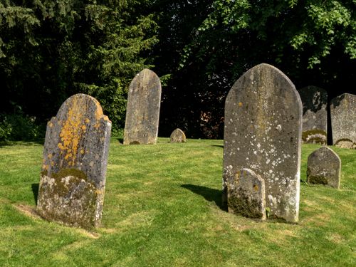 Free A serene cemetery scene with weathered tombstones standing on a lush green lawn under the shade of trees. Stock Photo