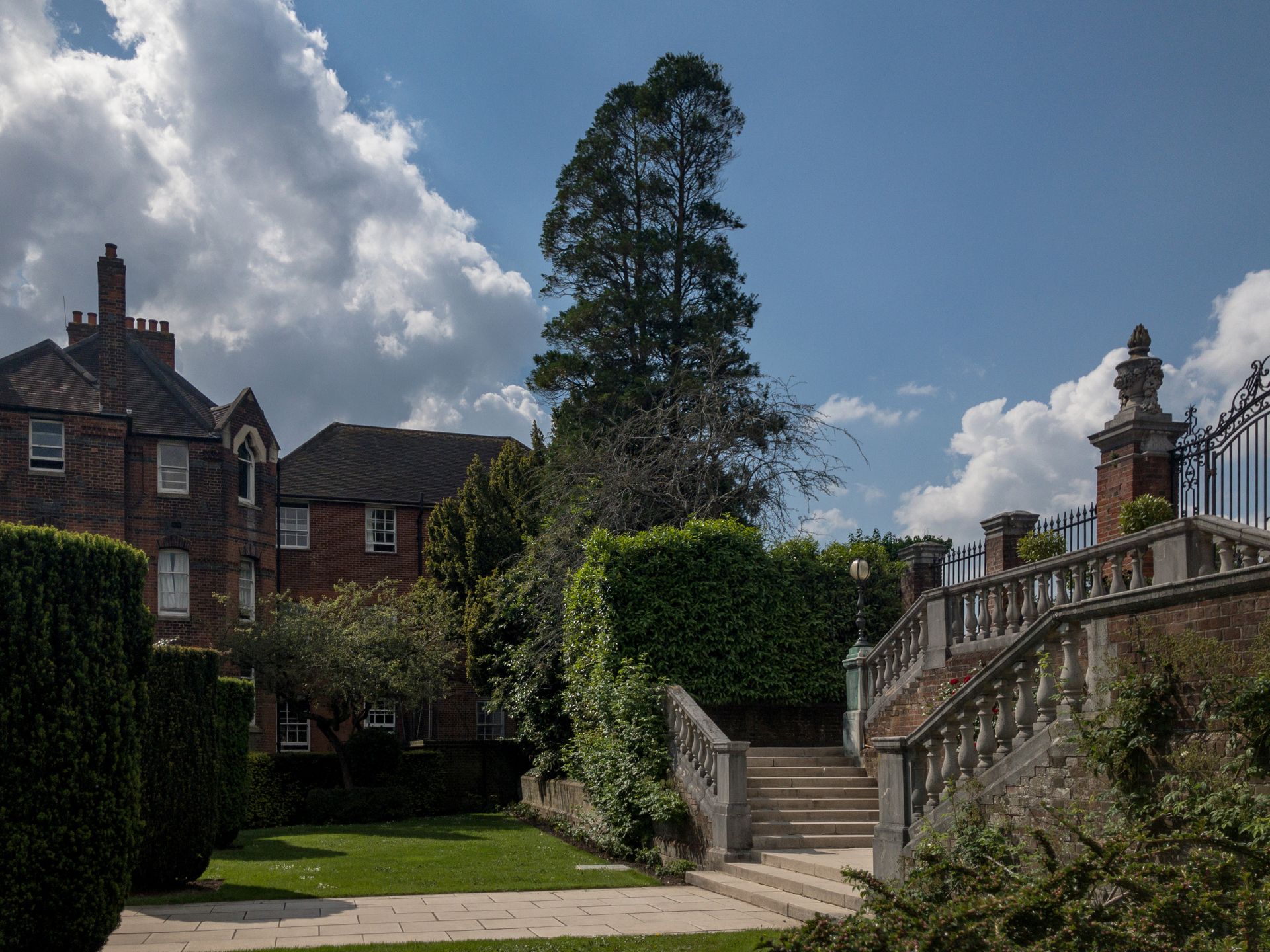 Charming old English garden with historic brick building and stone steps under a bright sky.
