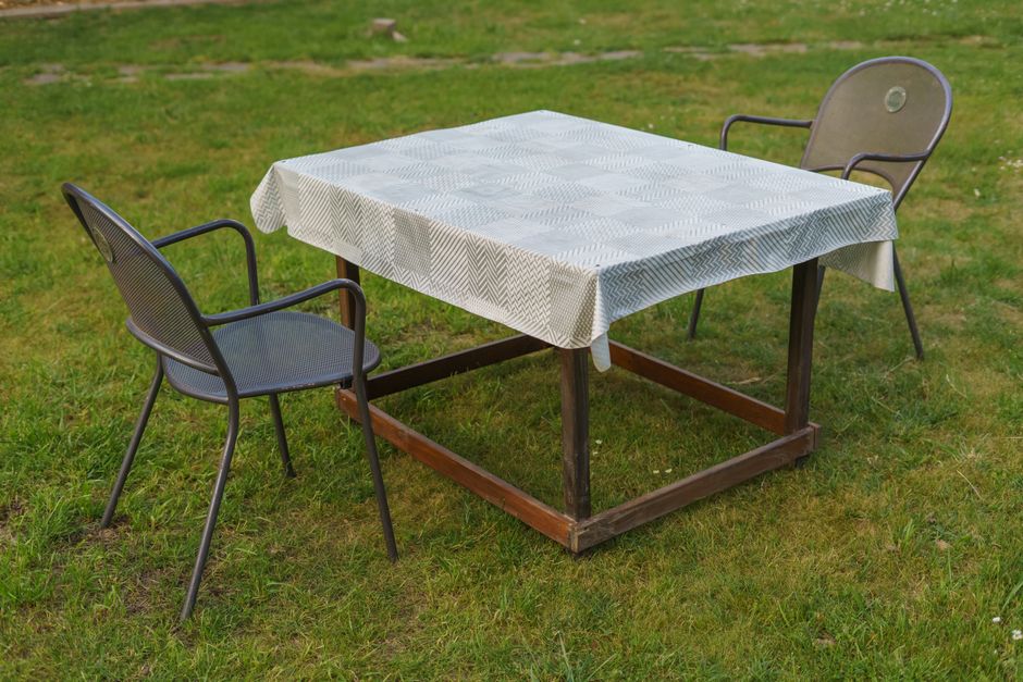 A tranquil outdoor setup with two metal chairs and a wooden table on a grassy lawn, perfect for al fresco dining.