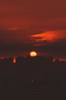 Silhouette of a city skyline with a vibrant orange sunset casting warm hues.