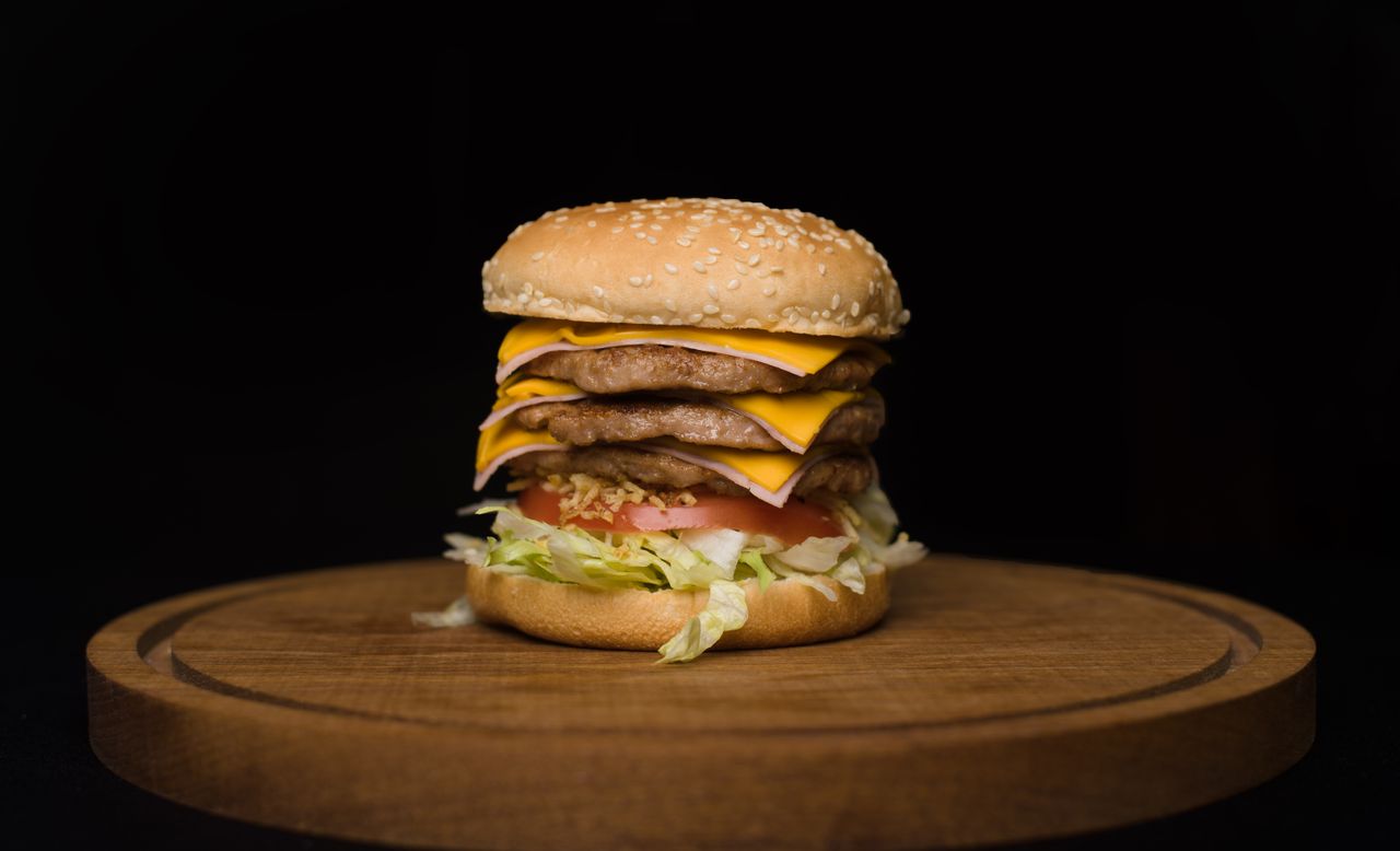 mouthwatering triple cheeseburger with lettuce and tomato on wooden tr