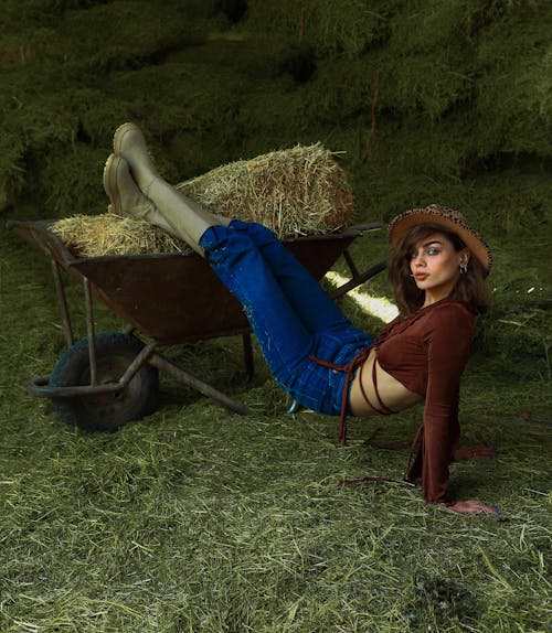 A woman laying on the ground with hay in a wheelbarrow