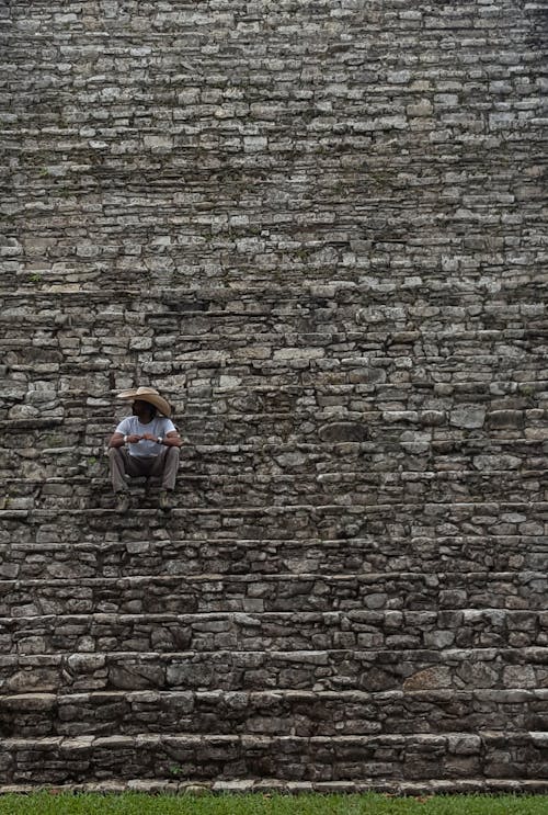 A man wearing a Sombrero is resting on the stairs of a pyramid, mexico.
