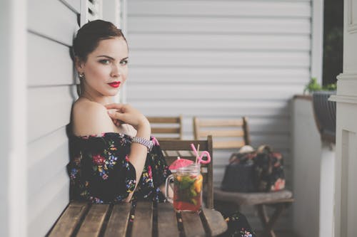 Woman Wearing Black Floral Off-shoulder Top Sitting on Wooden Chair