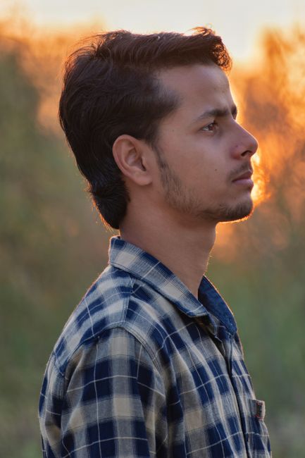 Side profile portrait of a young man outdoors at sunset in a plaid shirt.
