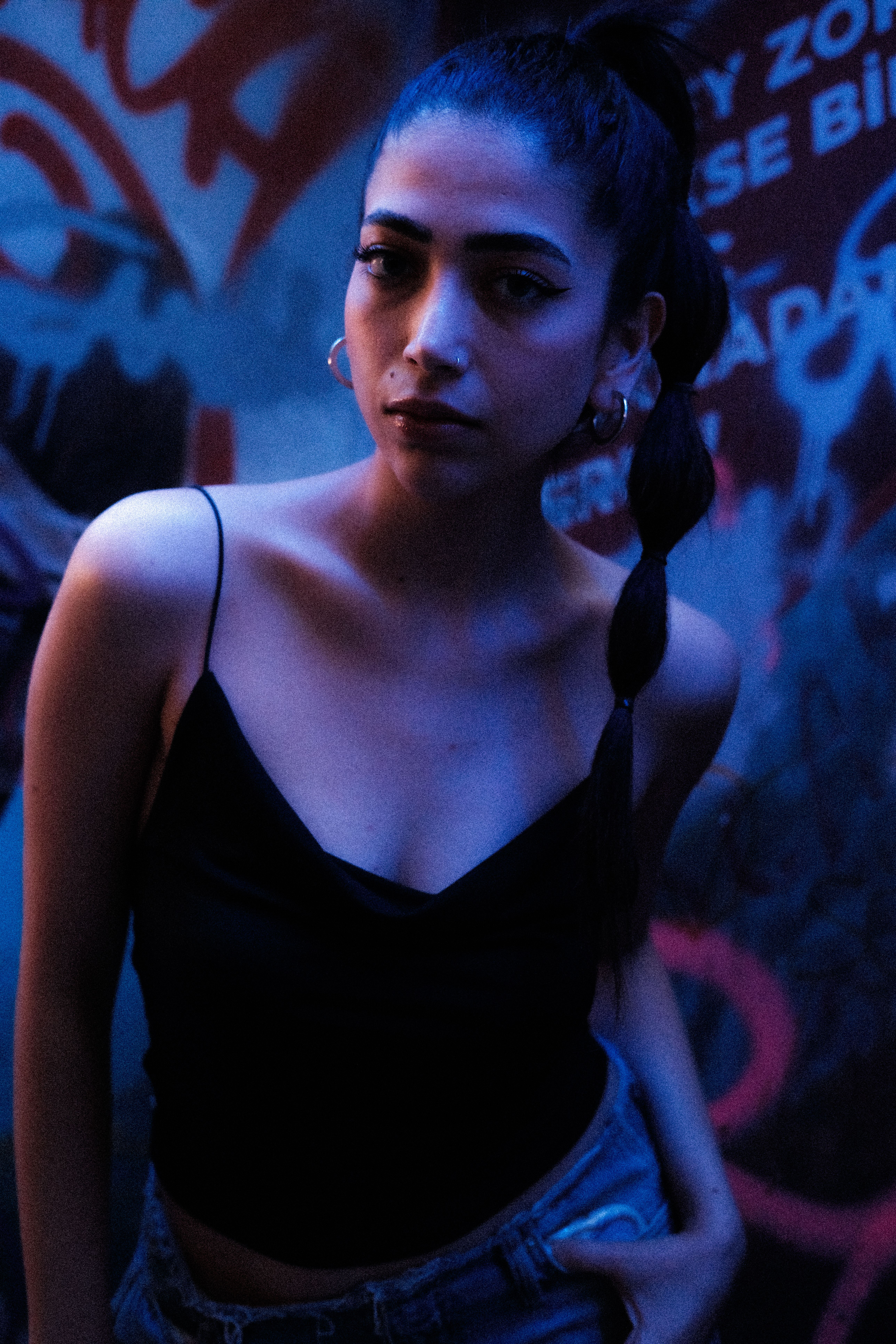 Stylish portrait of a woman with graffiti backdrop in moody nighttime lighting.