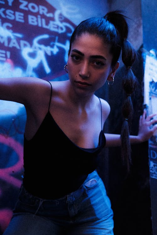 A woman in a black top and jeans leaning against a wall