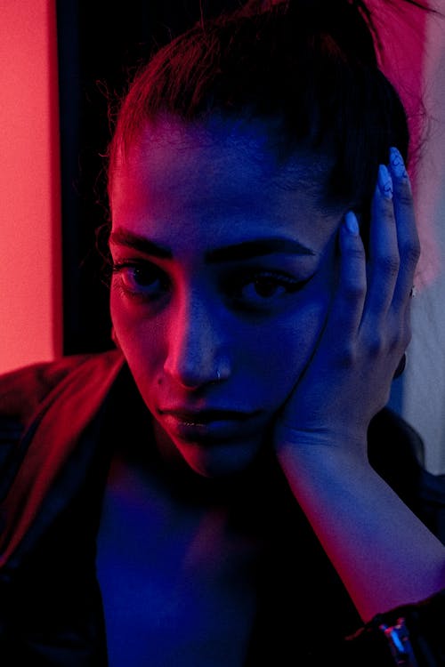 A woman with her hand on her head in front of a red and blue light