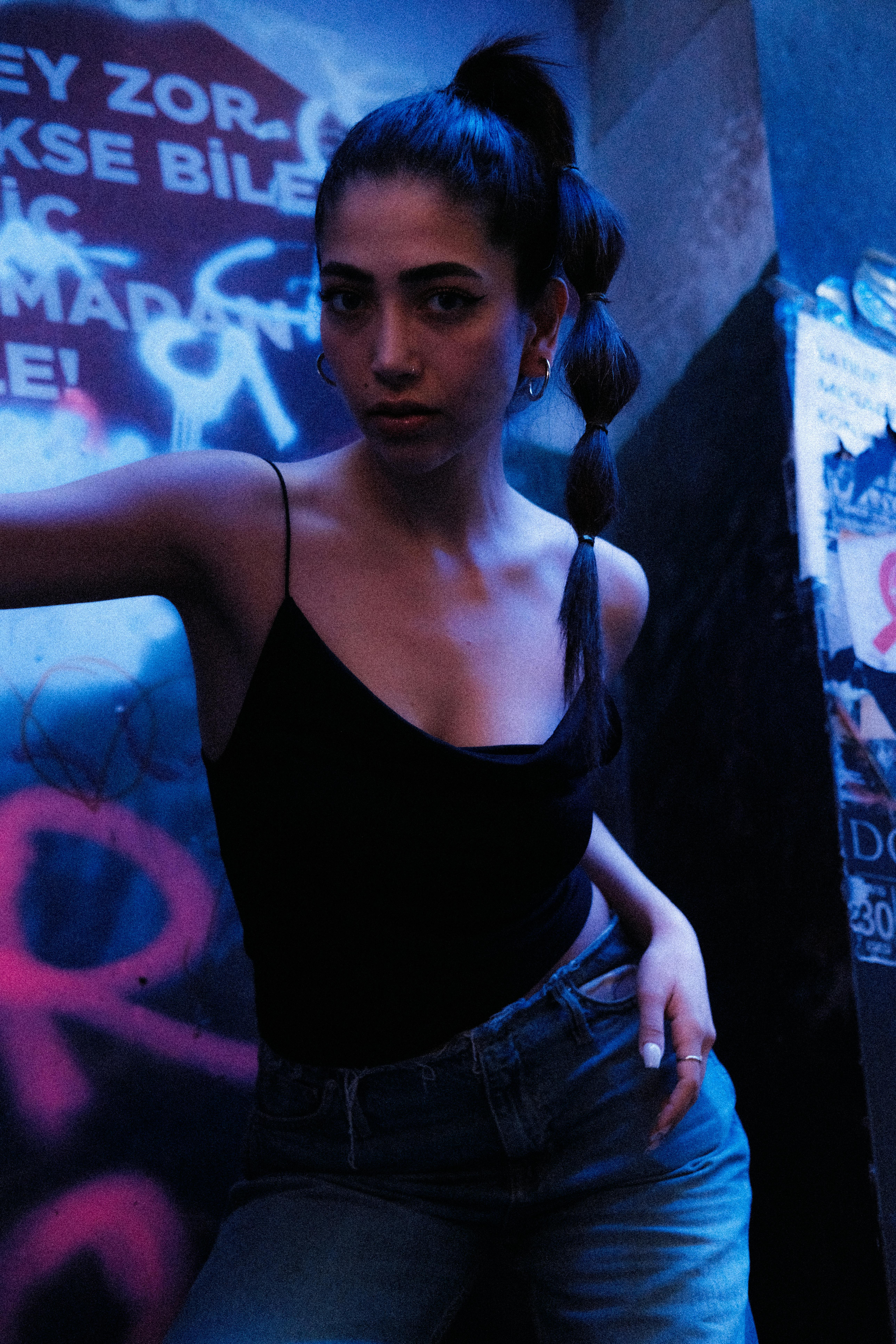 Stylish woman with a braid poses in a dimly lit urban environment.