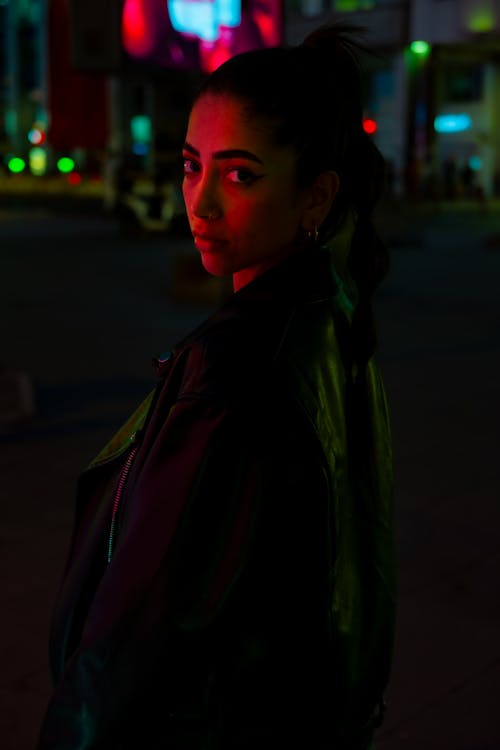 A woman in a leather jacket standing in front of a neon sign