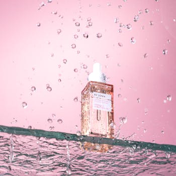A studio shot of an elegant cosmetic serum with water splashes on a pink background.