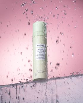 A cosmetic mist bottle with water splash isolated on a pink background.
