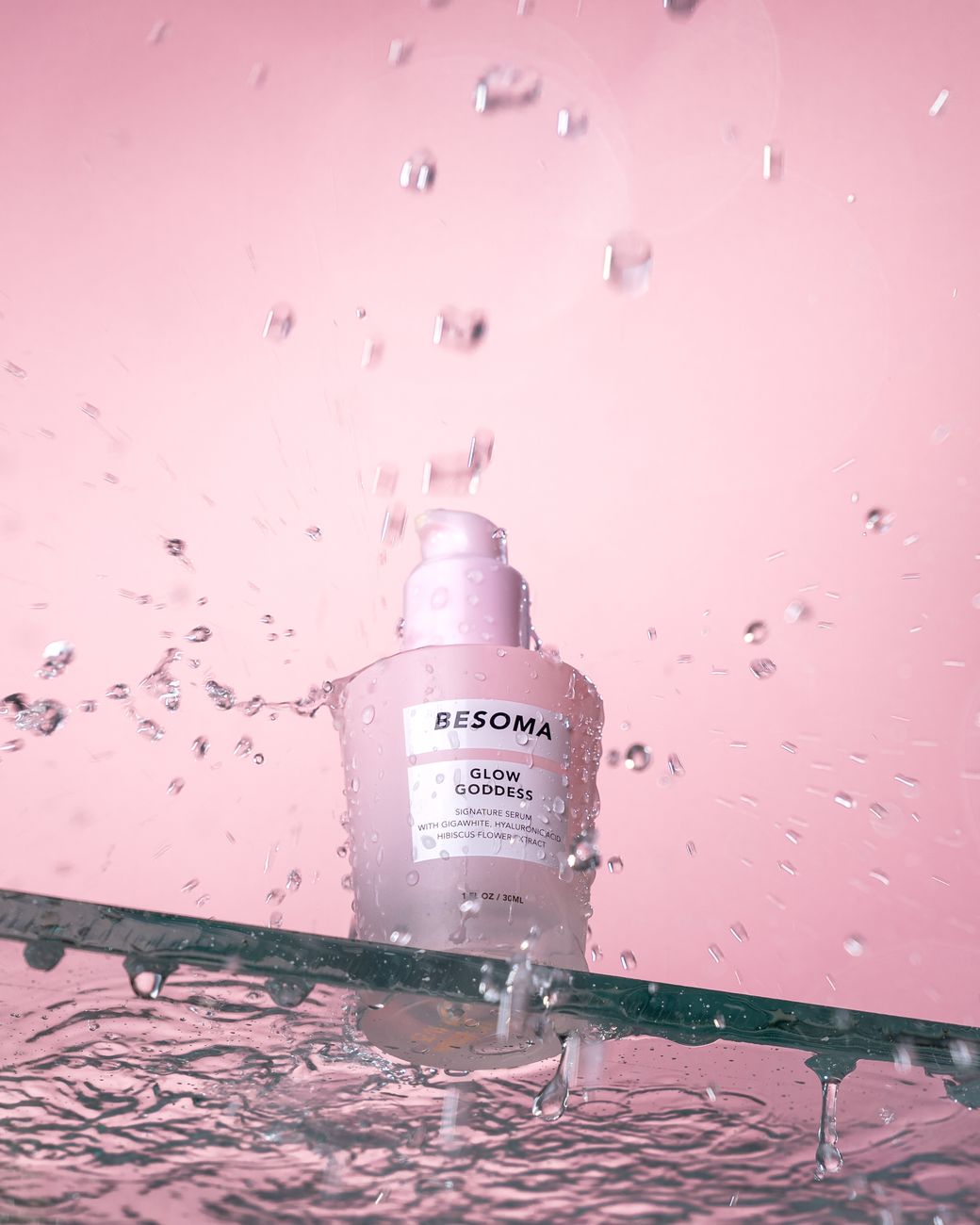 Pink background with skincare bottle and water droplets creating a refreshing and clean aesthetic.