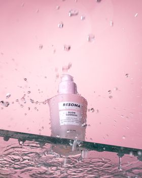 Pink background with skincare bottle and water droplets creating a refreshing and clean aesthetic.