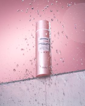 Vertical studio shot of a pink cosmetic bottle in water droplets, perfect for beauty and skincare themes.