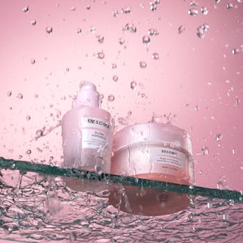 Dynamic display of skincare bottles on a glass shelf with cascading water in a pink setting.