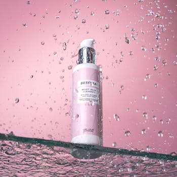 Besoma Milky Jelly Cleanser bottle with droplets against a pink background.